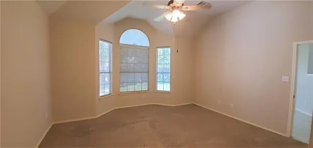 an empty room with a chandelier fan and windows
