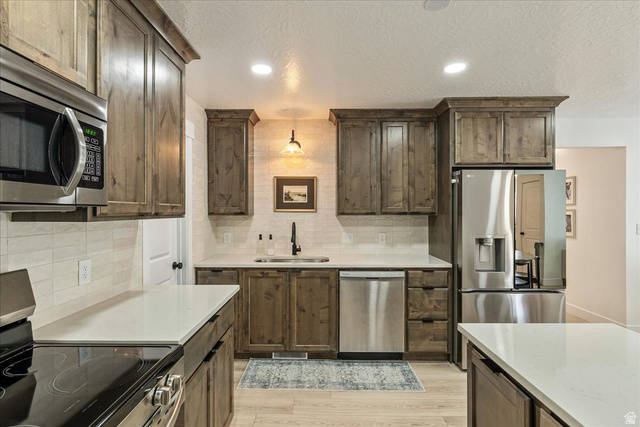 3916 South Sage Wood Avenue Mapleton, UT 84664 - Photo 11 of 33 Kitchen featuring wood-finish cabinetry, stainless steel appliances, light-toned countertops, tile backsplash, and light wood-finish flooring