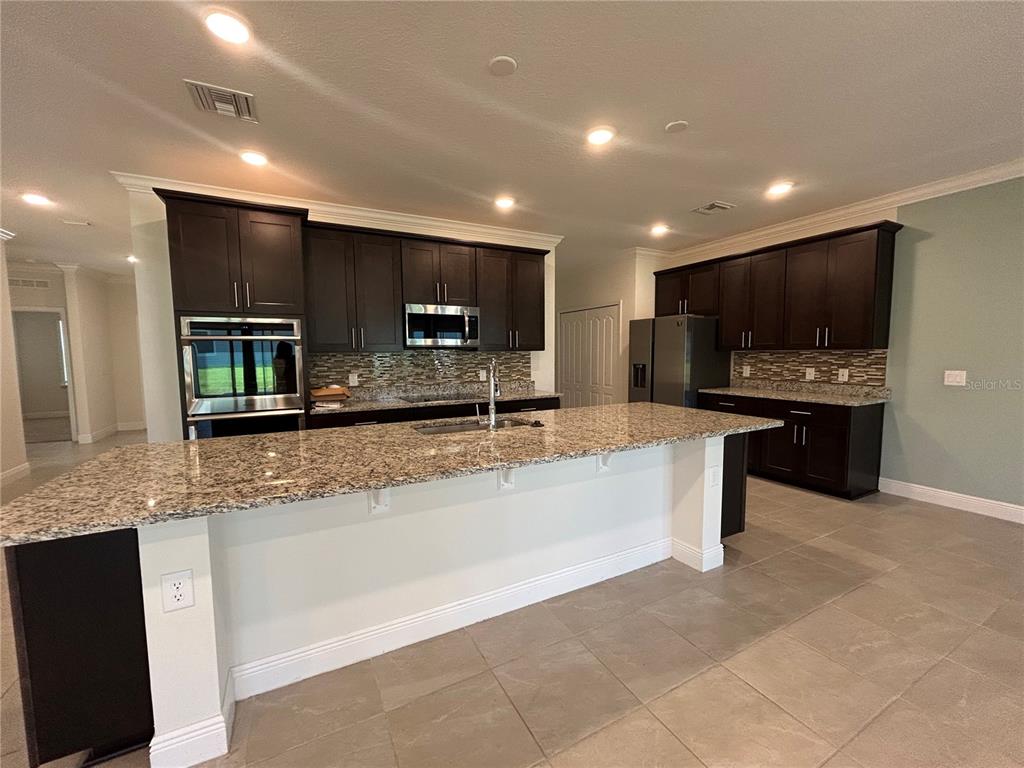 24470 Northwest 6th Road Newberry, FL 32669 - Photo 4 of 22 a large kitchen with stainless steel appliances a large counter top a stove a sink a refrigerator and a granite counter tops