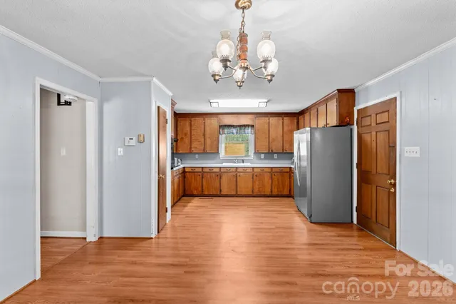 a view of a big room with wooden floor kitchen chandelier and a refrigerator