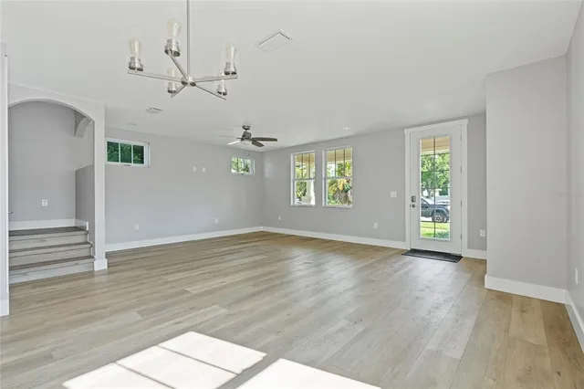 an empty room with wooden floor chandelier and windows