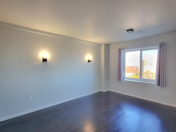 a view of an empty room with wooden floor and a window