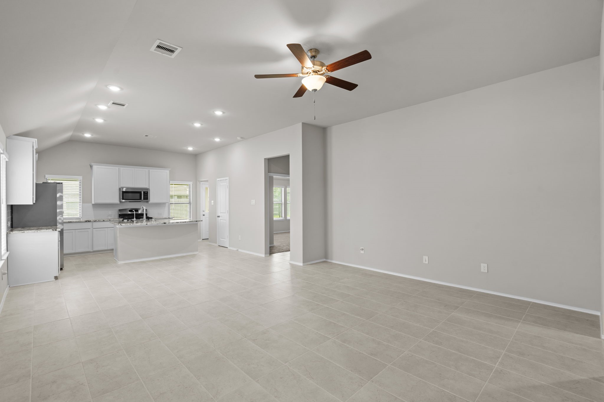 2011 Oak Leaf Court Manvel, TX 77578 - Photo 7 of 28 Open-concept living area features a modern kitchen with granite countertops and stainless steel appliances, adjacent to a spacious living room with tile flooring and a ceiling fan, perfect for comfortable living and entertaining.