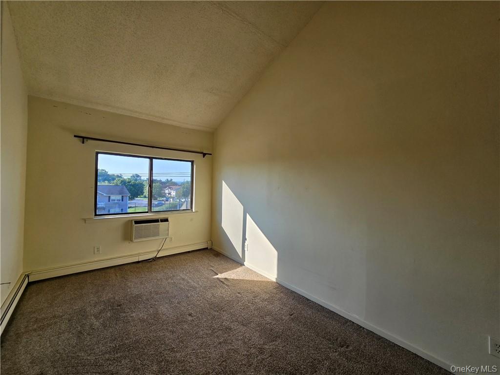 44 Inwood Road Middletown, NY 10941 - Photo 9 of 15 Empty room featuring a wall mounted AC, vaulted ceiling, baseboard heating, and carpet flooring