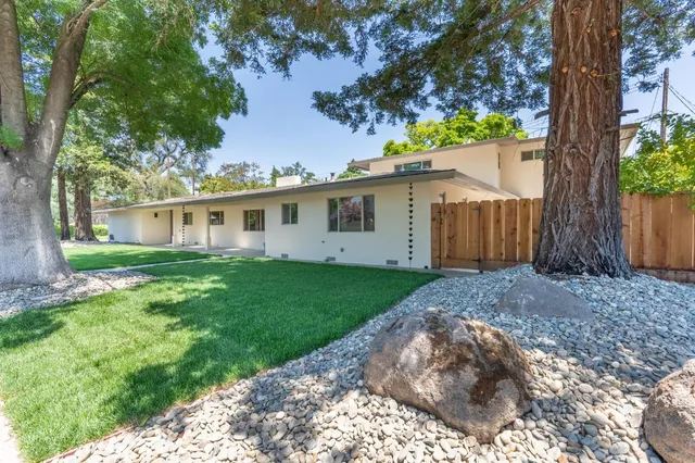 a view of a white house next to a yard with a large tree