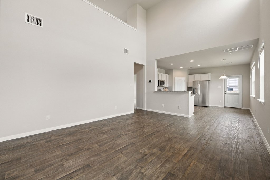 102 Ashford Way Georgetown, TX 78626 - Photo 5 of 28 A spacious living area with tall ceilings and elegant wood flooring connects seamlessly to a modern kitchen.