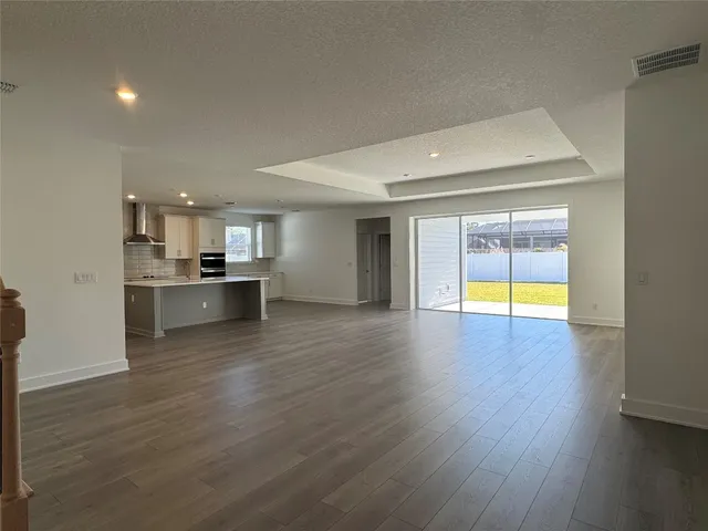 a view of empty room with wooden floor and kitchen view