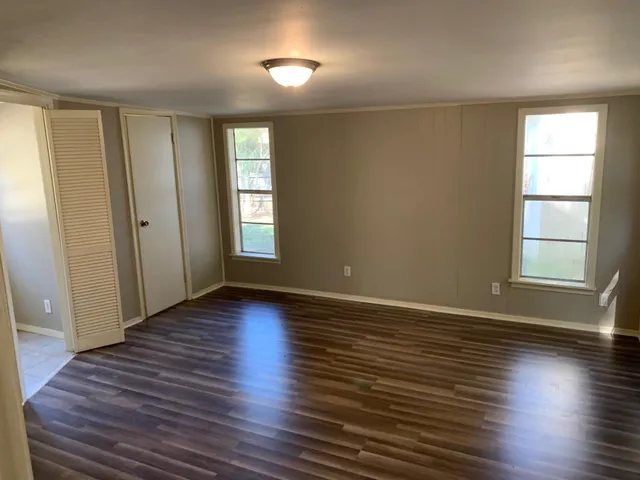 an empty room with wooden floor and windows with curtains
