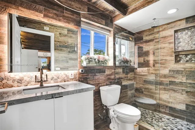 a bathroom with a granite countertop toilet a sink a mirror and a shower