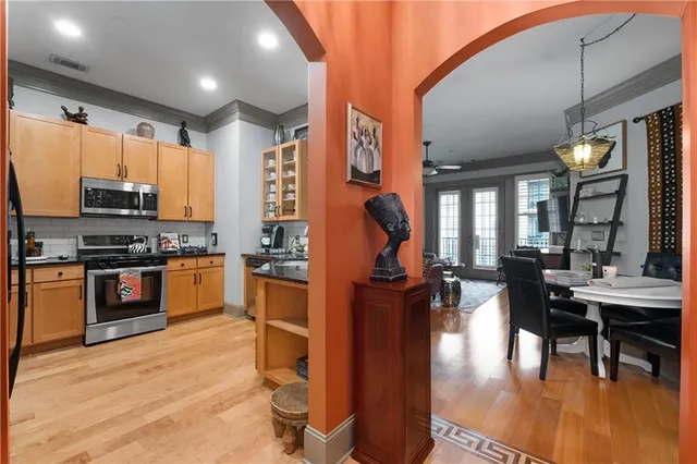 a kitchen with stainless steel appliances kitchen island granite countertop a stove a refrigerator a dining table and chairs with wooden floor