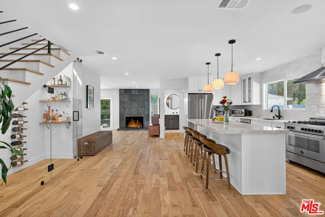 a kitchen with stainless steel appliances kitchen island granite countertop a stove a sink a refrigerator and white cabinets with wooden floor