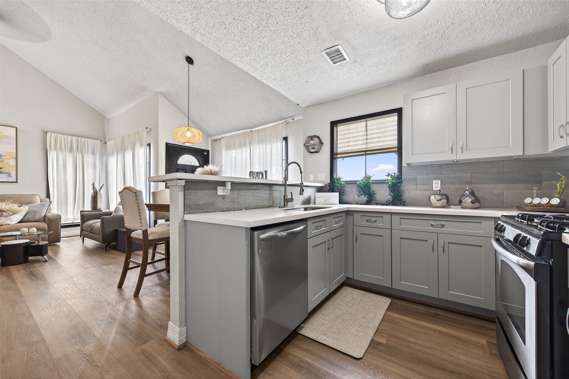 18446 North Willow Bluff Road Katy, TX 77449 - Photo 17 of 33 This photo showcases a bright, open-concept kitchen and living area. The kitchen features modern gray cabinetry, stainless steel appliances, and a stylish backsplash. The living area is well-lit with natural light from large windows and includes cozy seating, creating a welcoming atmosphere.