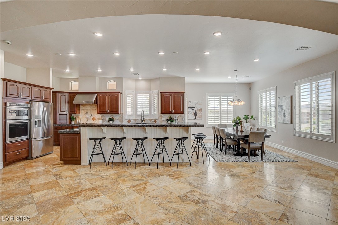 1182 Thomas Bay Circle Logandale, NV 89021 - Photo 20 of 98 Kitchen with appliances with stainless steel finishes, wall chimney range hood, a breakfast bar area, a chandelier, and backsplash