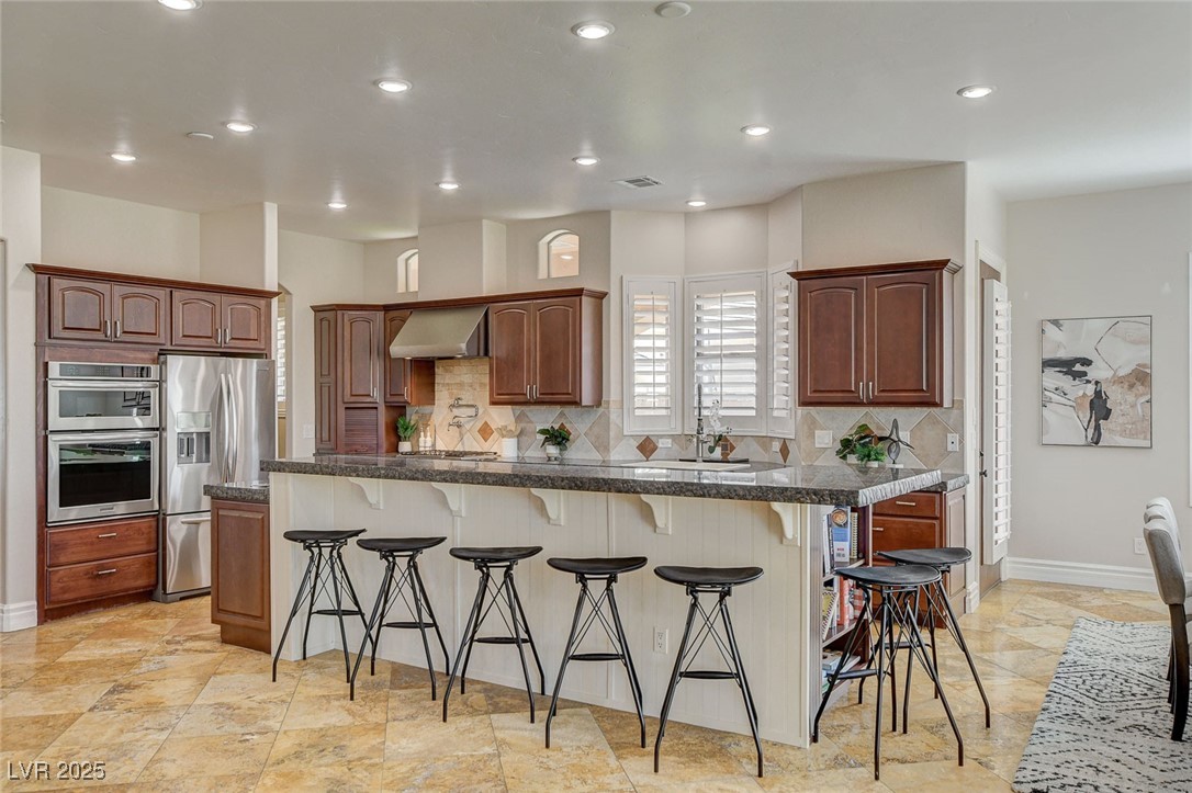 1182 Thomas Bay Circle Logandale, NV 89021 - Photo 22 of 98 Kitchen featuring appliances with stainless steel finishes, a breakfast bar, tasteful backsplash, hood, and recessed lighting