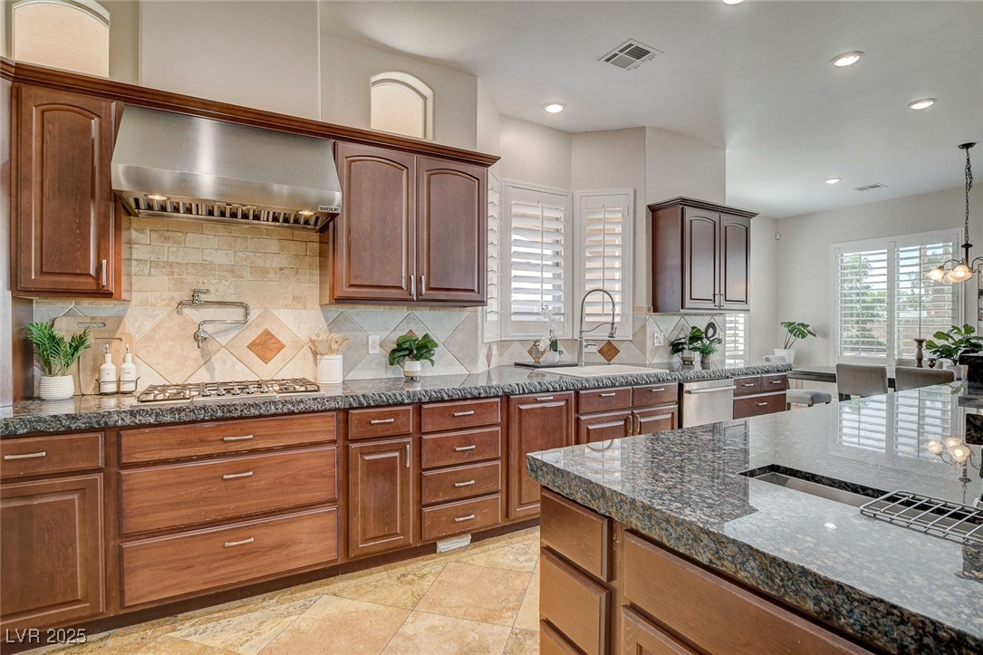 1182 Thomas Bay Circle Logandale, NV 89021 - Photo 27 of 98 Kitchen featuring wall chimney range hood, stainless steel appliances, dark stone countertops, tasteful backsplash, and recessed lighting