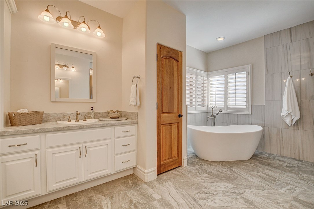 1182 Thomas Bay Circle Logandale, NV 89021 - Photo 73 of 98 Bathroom with marble look tiles, a freestanding bath, vanity, and tile walls