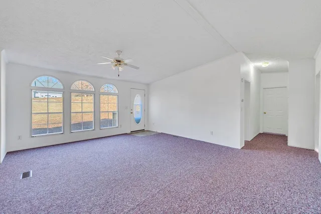 an empty room with chandelier fan and windows