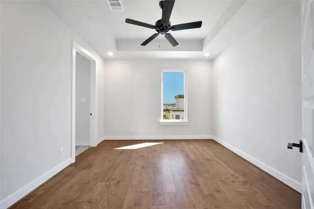 an empty room with wooden floor ceiling fan and windows