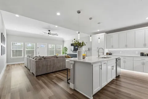 a living room with kitchen island granite countertop wooden floor and white cabinets