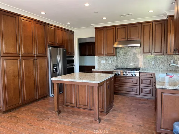 a kitchen with stainless steel appliances kitchen island granite countertop a stove a refrigerator and a sink with wooden cabinets