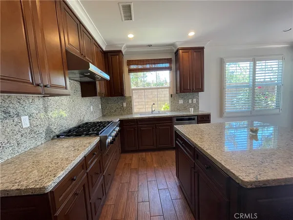 a kitchen with granite countertop kitchen island wooden floors wooden cabinets a sink a window and appliances