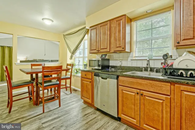 a kitchen with stainless steel appliances granite countertop wooden cabinets a sink a stove a dining table and chairs