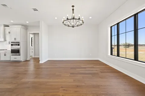 an empty room with wooden floor chandelier and window