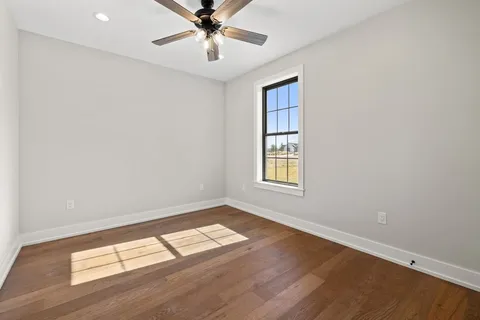 an empty room with wooden floor chandelier fan and windows