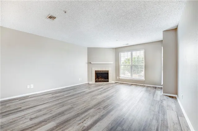 a view of an empty room with wooden floor fireplace and a window