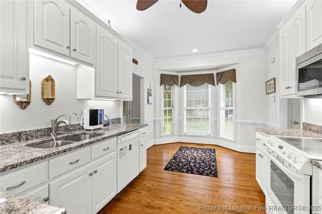 a large white kitchen with granite countertop a stove a sink a window and white cabinets