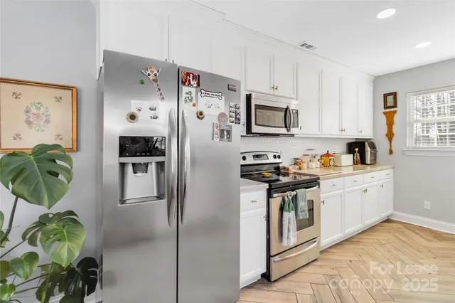 a kitchen with stainless steel appliances a stove a refrigerator sink a microwave a refrigerator and white cabinets