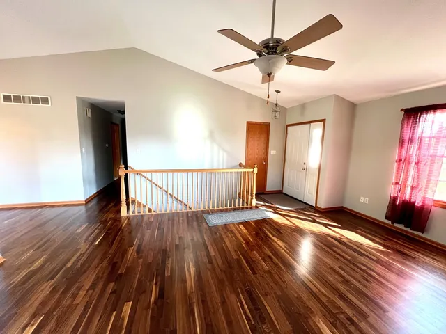 a view of an empty room with wooden floor and a ceiling fan