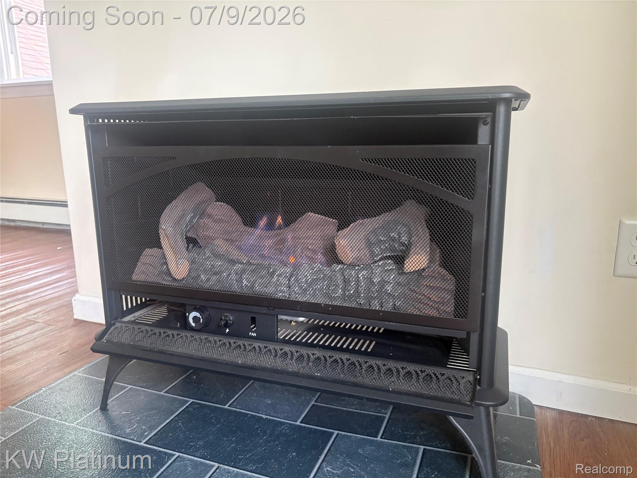 7280 North Road Fort Gratiot, MI 48059 - Photo 30 of 40 Freestanding gas fireplace with a black metal mesh screen, faux log insert, and stone-look tile hearth