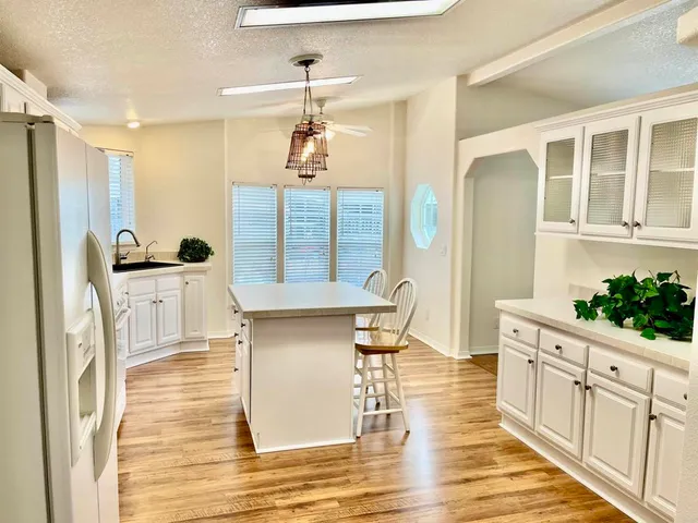 a open kitchen with stainless steel appliances kitchen island granite countertop a refrigerator a stove and white cabinets with wooden floor