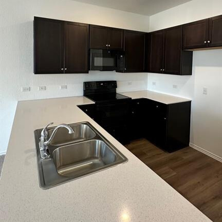 340 The Bad Way Jarrell, TX 76537 - Photo 9 of 14 Kitchen featuring black appliances, dark wood-style floors, light countertops, and dark brown cabinetry
