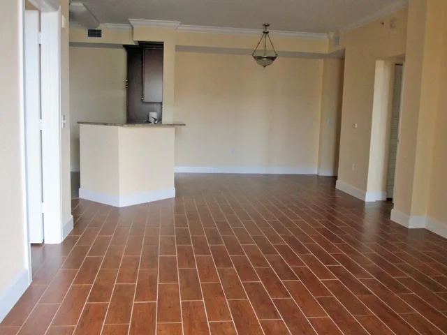 a view of an empty room with wooden floor and a kitchen