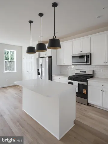 a kitchen with stainless steel appliances granite countertop a stove top oven a sink a refrigerator and white cabinets with wooden floor