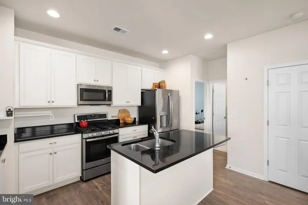 a kitchen with stainless steel appliances granite countertop a sink a stove a refrigerator and white cabinets