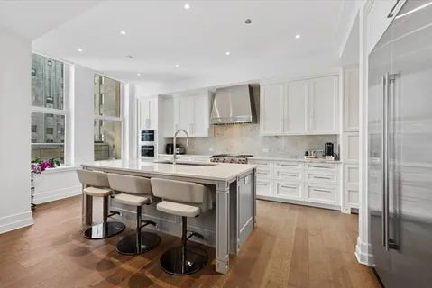 a kitchen with stainless steel appliances kitchen island granite countertop a stove a sink a refrigerator and white cabinets with wooden floor