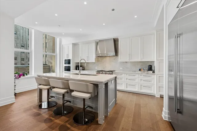 a kitchen with stainless steel appliances kitchen island granite countertop a stove a sink a refrigerator and white cabinets with wooden floor