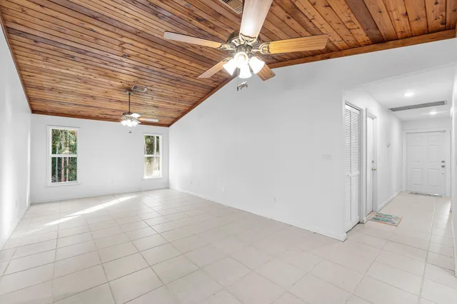 an empty room with wooden floor chandelier fan and windows