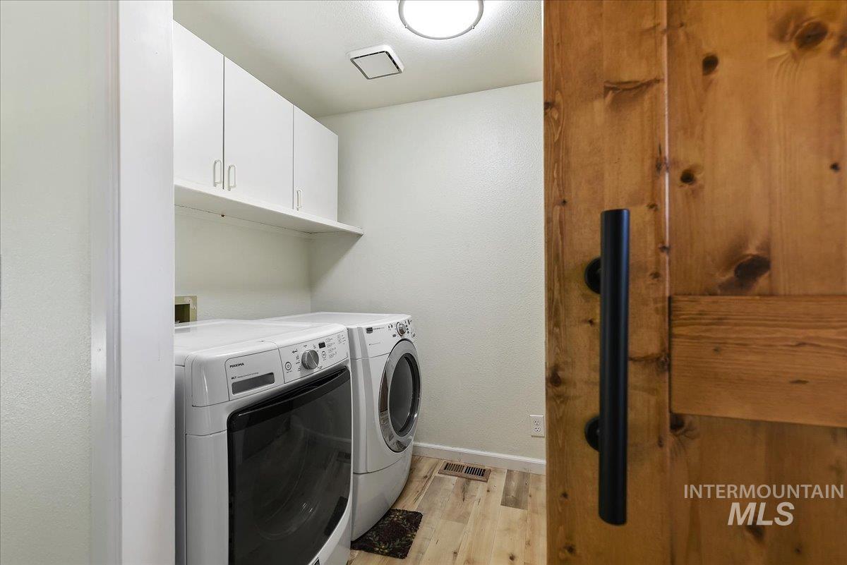 9215 West Preece Street Boise, ID 83704 - Photo 17 of 22 Dedicated laundry area featuring wood-finish flooring, white cabinetry with upper storage, and a natural wood door with a matte black handle