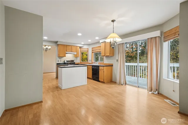 a kitchen with stainless steel appliances granite countertop a stove top oven a sink dishwasher a refrigerator and a dining table with wooden floor