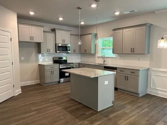 a kitchen with kitchen island granite countertop wooden floors stainless steel appliances and sink