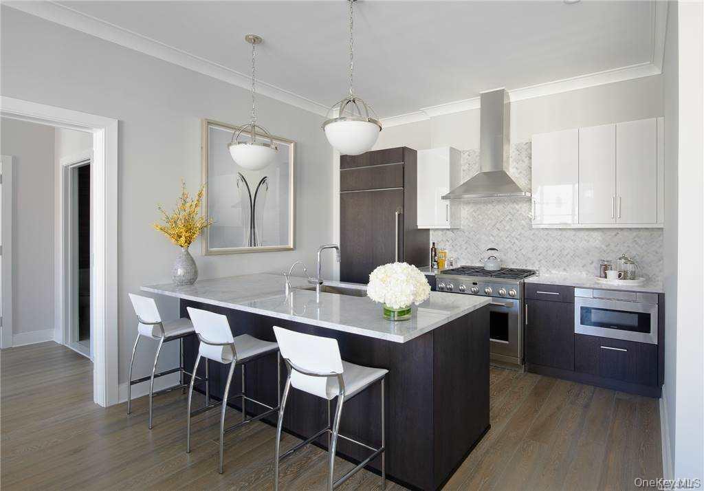 100 Garvies Point Road, Unit 1202 Glen Cove, NY 11542 - Photo 6 of 14 Kitchen featuring backsplash, a breakfast bar area, wall chimney range hood, dark brown cabinetry, and dark wood-type flooring