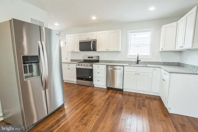 a kitchen with stainless steel appliances granite countertop a refrigerator a sink dishwasher a stove and white countertops with wooden floor