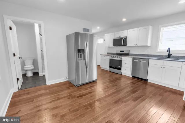 a large kitchen with stainless steel appliances granite countertop a stove top oven a refrigerator and white cabinets with wooden floor