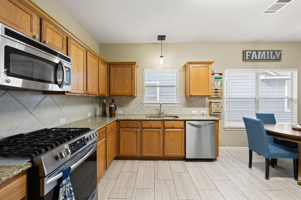207 Rosedale Boulevard Georgetown, TX 78628 - Photo 12 of 30 Kitchen with stainless steel appliances, light stone countertops, hanging light fixtures, and brown cabinetry