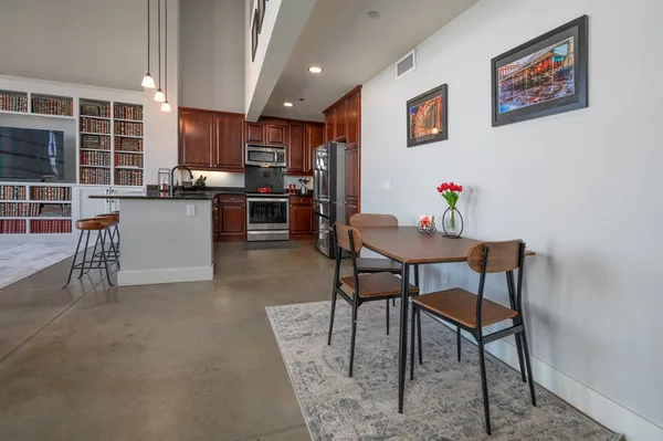 a kitchen with stainless steel appliances kitchen island granite countertop a dining table chairs and a refrigerator
