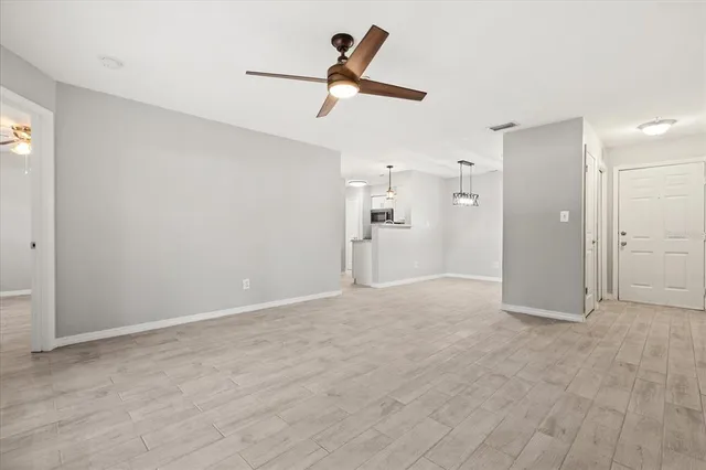 an empty room with ceiling fan and kitchen view